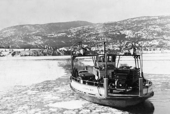 A boat carrying two cars on a body of water. 