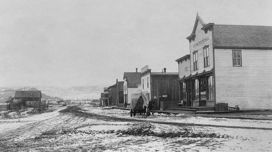A cart on a dirt pathway surrounded by a few wooden buildings.