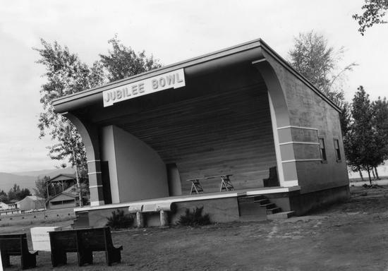 An outdoor stage with a table in its centre. Benches face the stage. Text: Jubilee Bowl