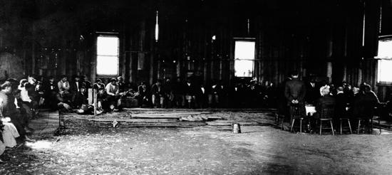The McKenna–McBride Royal Commission held its hearings in various locations in Clayoquot Sound in the spring of 1914, hearing testimony from aboriginal leaders as they argued for more land for their people. This scene shows the hearings on May 18,  1914, at Maaqtusiis. “My people are not going away from the places where they used to live,” declared Chief Billy, during his long and powerful testimony.
