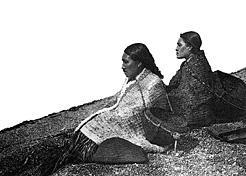 Nootka women on the beach with clam baskets on their backs, awaiting the tide to fall and uncover the clam beds. BC Archives D-08313